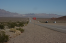 Streetside photo of a highway going through an empty desert landscape with mountains in the background.