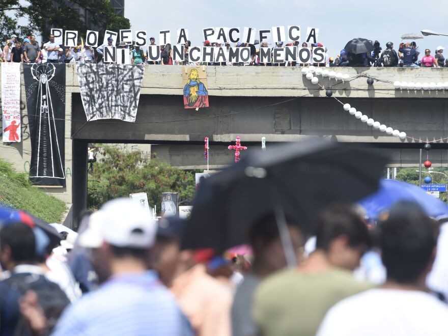 Protesters display signs from an overpass Monday in Caracas as they call for Maduro's ouster. The president blames the unrest — and the economic troubles that helped inspire it — on foreign powers like the U.S.