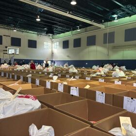 Rows of boxes situated next to each other in a gymnasium with a basketball hoop at the far left