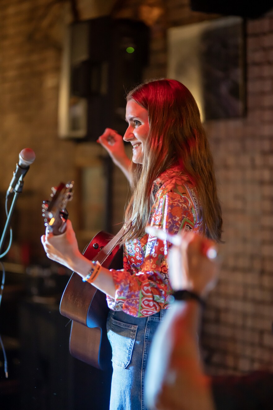 A smiling young woman seen from the side playing guitar