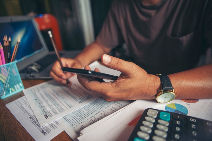 A man holds a pencil and calculator at a desk.