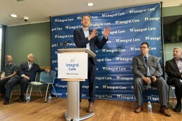 A photo of Travis County Judge Andy Brown standing a podium that has a sign on it with the words "Integral Care."