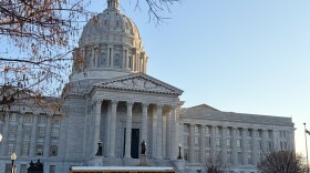 A yellow school bus is pulled up in front of the Missouri State capitol building. 