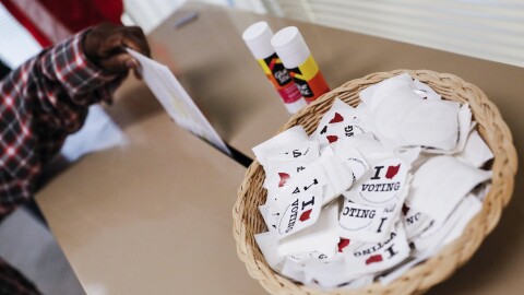 A voter in Hamilton County places their ballot in a ballot box next to a basket of "I Voted" stickers.