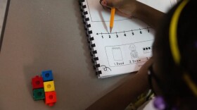 A young student works on a math problem on a worksheet using different colored linking blocks.