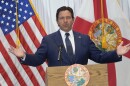 A man in a suit speaks at a podium during a press conference with arms spread wide