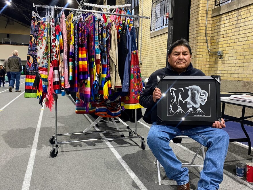 Leon Anthony holding one of his art pieces in front of his vendor at USU's 47th annual Powwow.