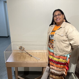 Photo of Monica Jo Raphael next to a rattle she made with porcupine quills