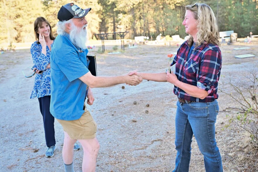 Elk Cemetery Commission challenger Steven Queener, left, shakes hands with incumbent Commissioner Rebecca Shannon Wednesday, Sept. 24, 2025, at Elk Cemetery as Queener’s campaign health care consultant, Dr. Bernadine Bank, smiles.