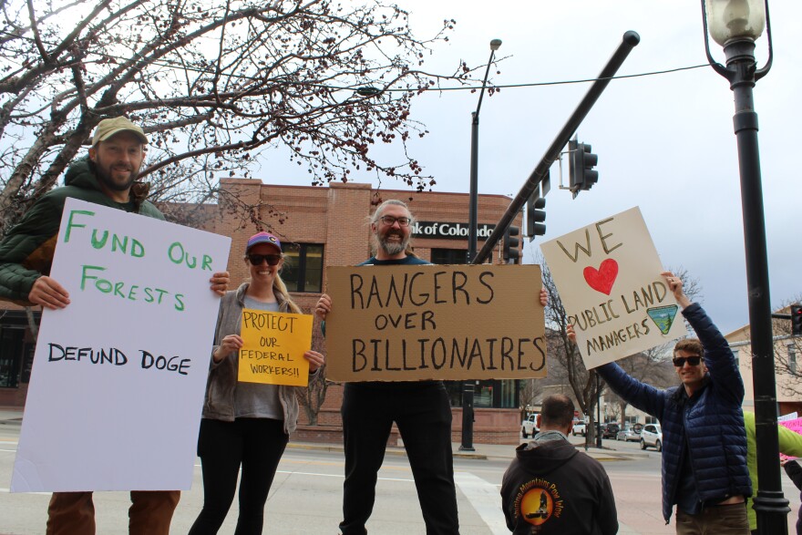 Sheeghan Meagher (left) holds a sign that says “Fund our forests, defund DOGE,” referencing Elon Musk’s “Department of Government Efficiency” task force. Other signs say “Protect our federal workers,” “Rangers over billionaires,” and “We love public land managers.”