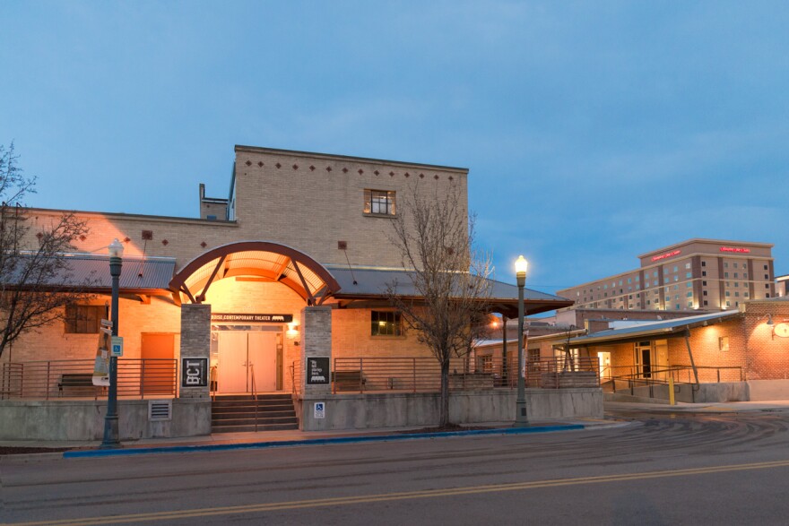 The outside of a tan building, which has concrete steps leading up to a large patio area and double steel doors. 