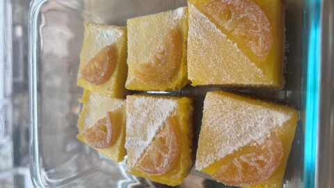 A clear pyrex plate of lemon bars with powdered sugar ana a lemon slice.