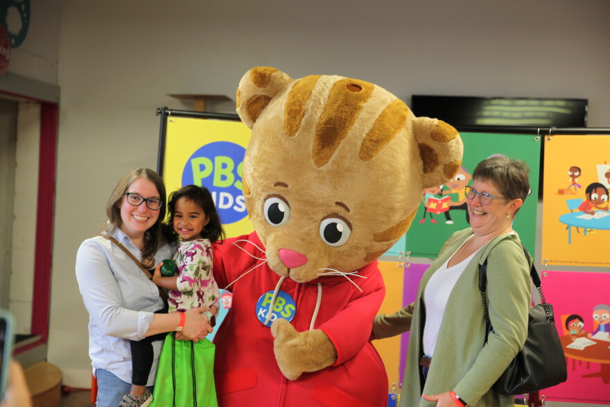 Visitors pose with Daniel Tiger in front of colorful hanging tiles.
