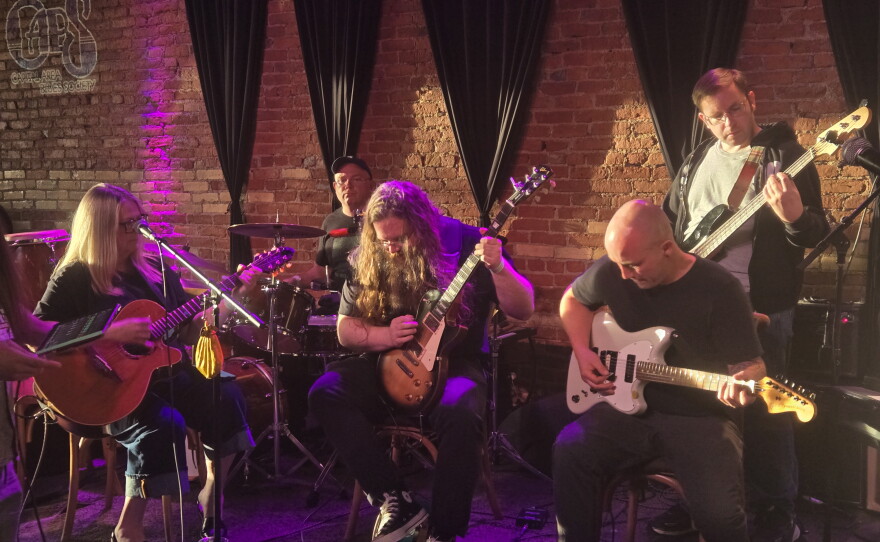 Several guitar and bass players on stage with a drummer in the back