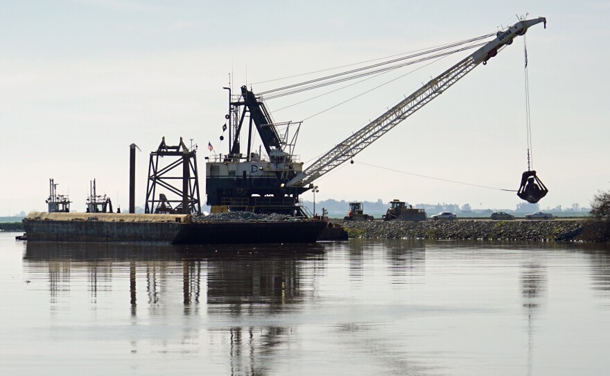 A dredge drops rocks onto a damaged levee in California's delta.