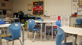 An empty classroom with round desks and blue plastic chairs around them