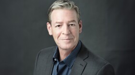 Roy Kaiser smiles in front of a gray background