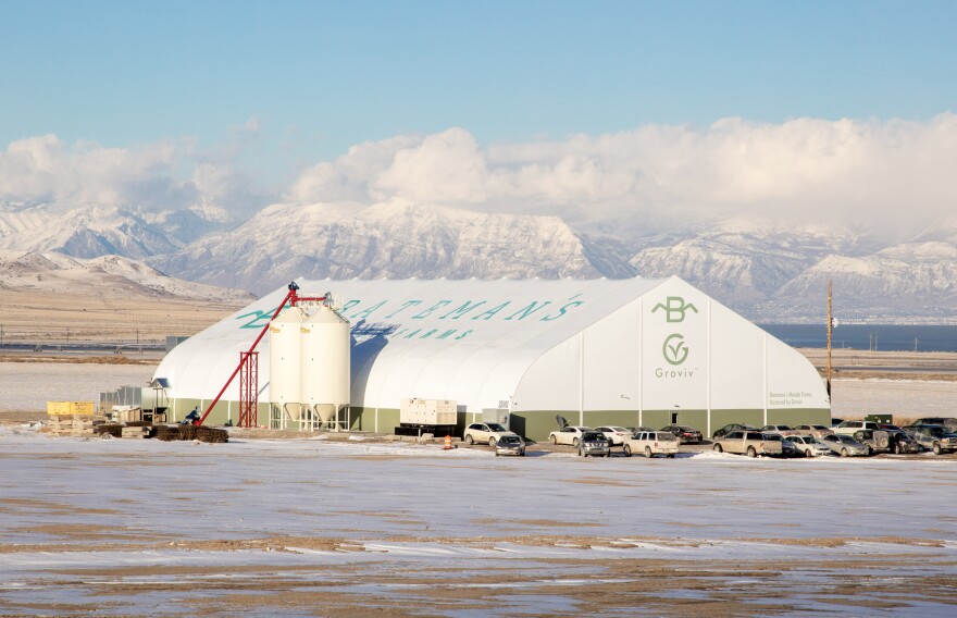 A large white hanger-like structure sits on a snowy field. Snow capped mountains are visible in the background.