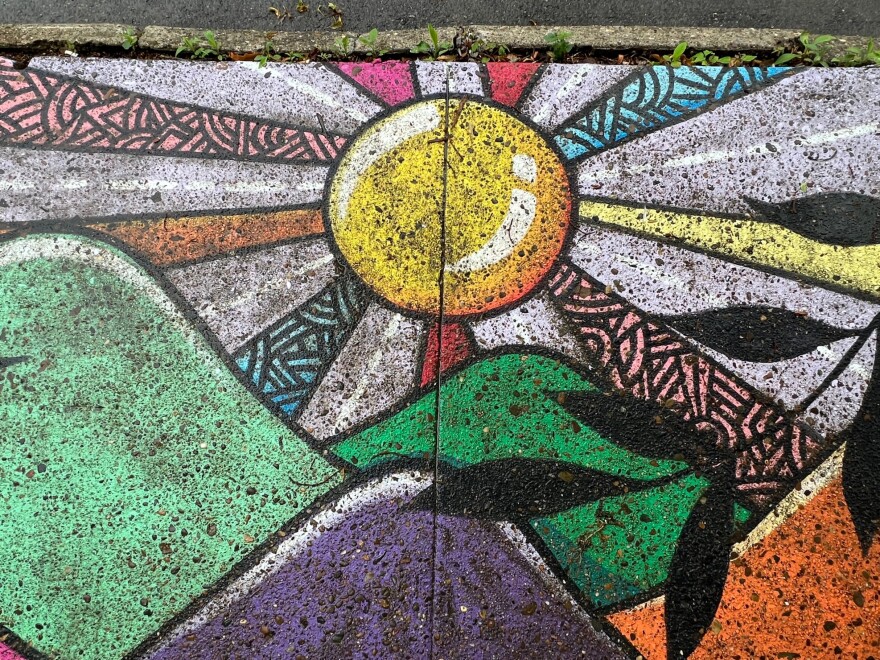 A sunrise with colorful, patterned rays is painted onto sidewalk squares.