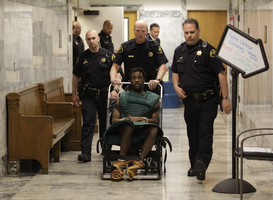 Accused rapist and murderer Isaiah Kalebu is taken in a wheeled restraint chair through a hallway at the King County Courthouse in May. He was not allowed in court Monday, the first day of his trial.