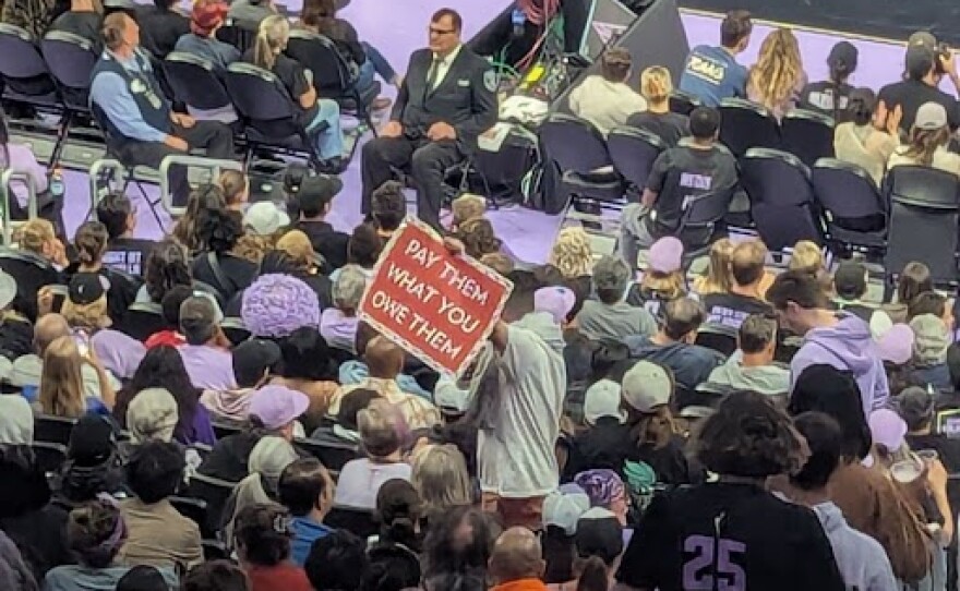 Person holding a pay them what you owe them sign at a Golden State Valkyries Game