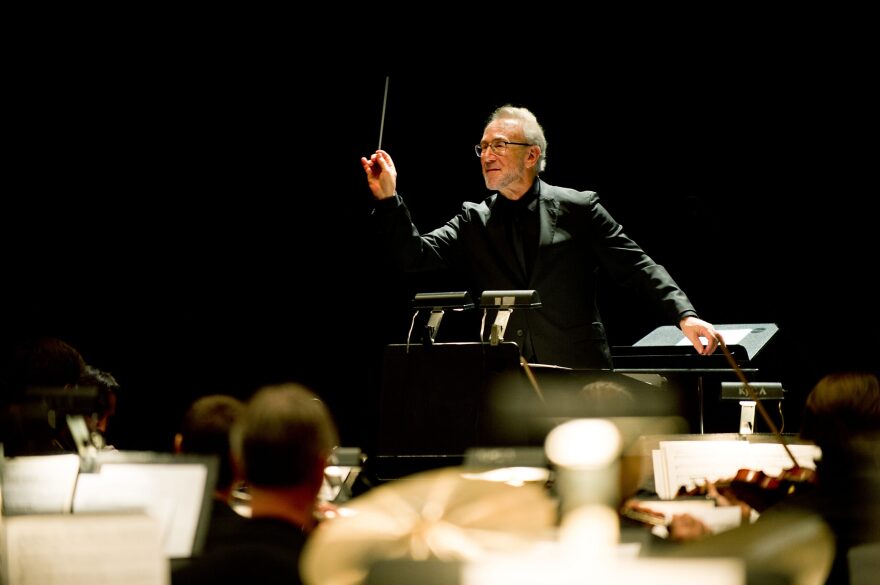 Louisville Orchestra Pops conductor Bob Bernhardt wearing an all-black suit, holding a baton on the podium during a performance, directing music 