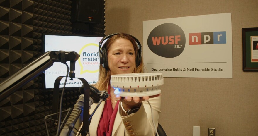 Woman sits near mic holding a sensor in her hand 