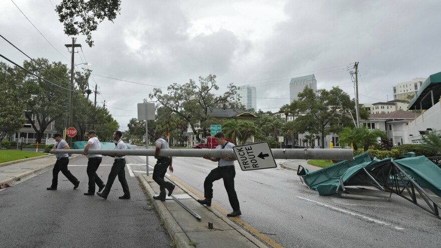 Members of Tampa Fire Rescue remove a street pole after large awnings from an apartment building blew off from winds associated with Hurricane Idalia Wednesday, Aug. 30, 2023, in Tampa. Idalia made landfall earlier in the day hundreds of miles away along the Big Bend of the state.