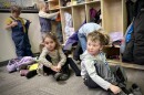 Four kids take off their winter clothes inside a classroom.
