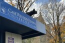 Case Western Reserve University sign atop a kiosk for posting bills against a backdrop of autumn leaves and a brick building.
