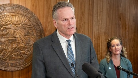 Man speaking into microphones in wood-paneled room