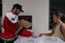 A student wearing a backpack hands a phone over to an adult in a hockey jersey standing behind multiple bins.