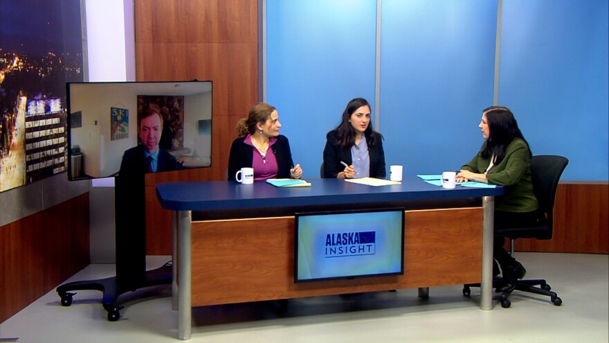 3 people sit around a desk, another joins them on a TV over Zoom.