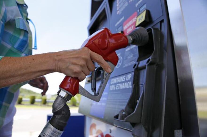 Closeup of a gas pump. You can see the arm of a person putting the nozzle back into the pump. It's a sunny day outside. 