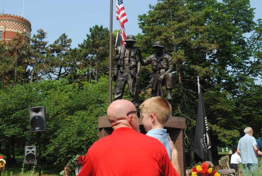 A man kneels beside his son after placing small flags at the base of the monument following the Memorial Day ceremony in 2012.