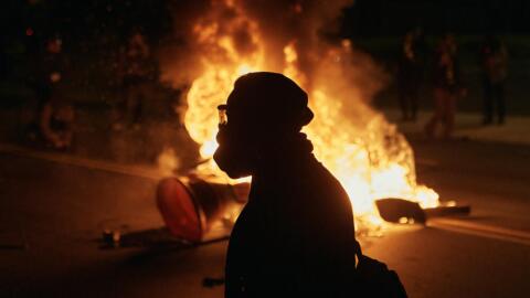 A man wearing protective gear walks in front of a burning barricade outside the Delaney Hall detention center during a protest against the transfer of detainees and federal immigration policies on Saturday, May 30, 2026, in Newark, N.J. (Andres Kudacki/AP)