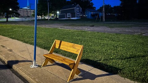 A wooden bench sits on a sidewalk next to a bus stop pole