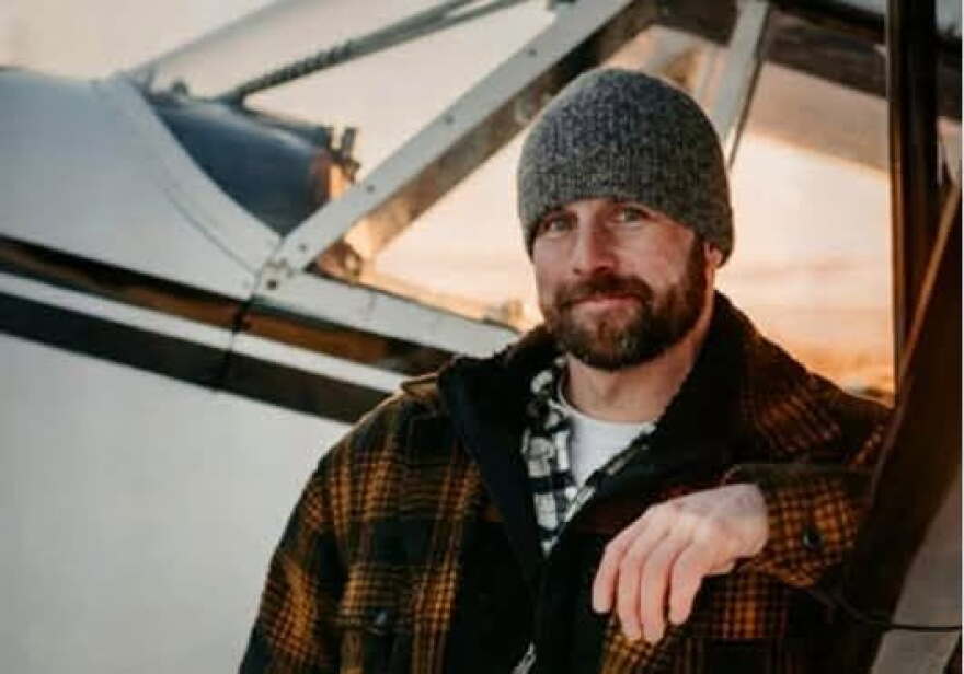 A man in a gray beanie looks into the camera while standing in front of a closely cropped small airplane.