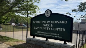 A sign for Christine W. Howard Park and Community Center stands beside a sidewalk and fenced recreation area.
