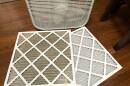 A box fan sits on the floor next two two air filters: one dirty and one clean