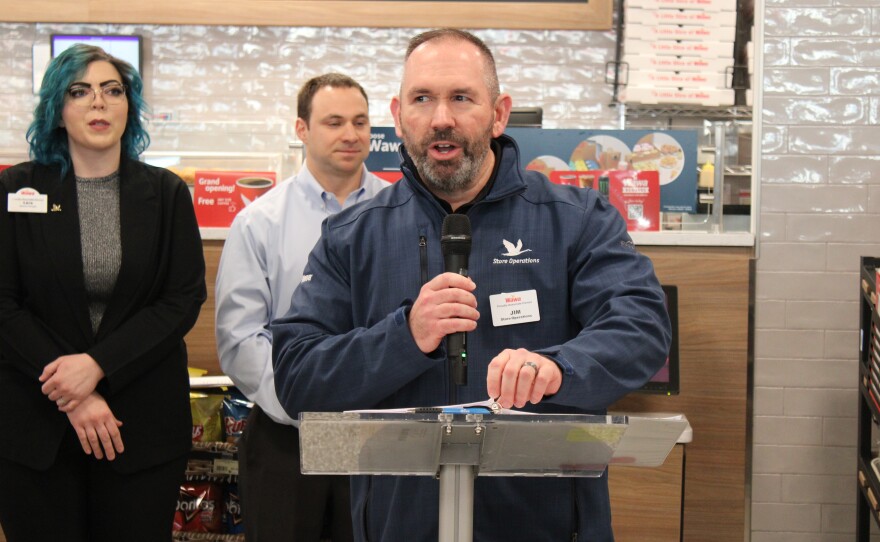 Director of Store Operations Jim McGee speaks at a podium inside the new Wawa. The store's Area Manager Cody Lilly and General Manager Lara Faine-Cribb stand behind McGee.