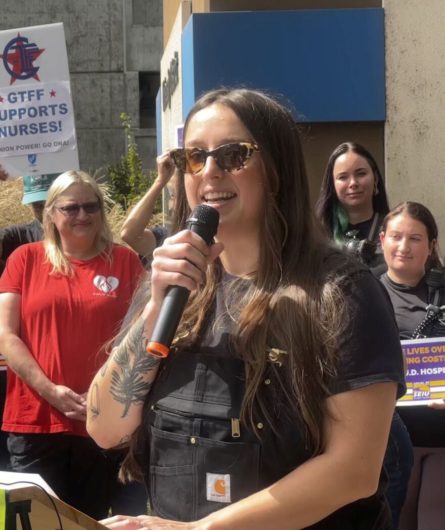 Woman holding microphone at podium, with crowd behind her. 