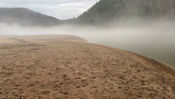 A barren muddle landscape shrouded in fog. Beneath the fog, barely visible, is Gatewood lake. In the background is forest.