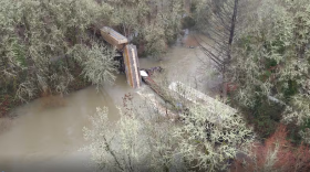 A collapsed railroad trestle with train cars in a river.