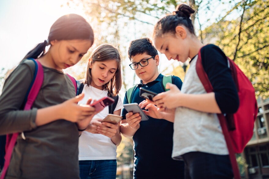 Group of kids hang out in the street after school and using smart phones on a sunny day