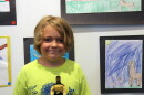 J.R. Patterson stands in front of a wall of art. He has medium length dirty blond hair, is wearing a neon yellow shirt and is holding a Star Trek action figure.