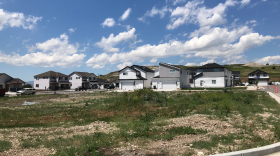 A row of houses leading into a cul-de-sac across a patchy field of grass.
