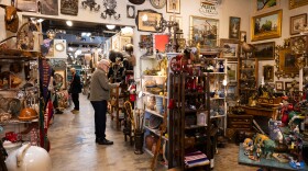 People look at objects in a store that is crowded with antique looking items.