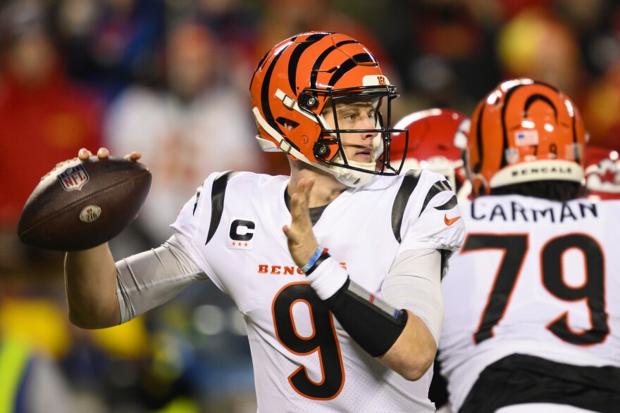 joe burrow, wearing a white bengals jersey and an orange and black helmet, throws a football