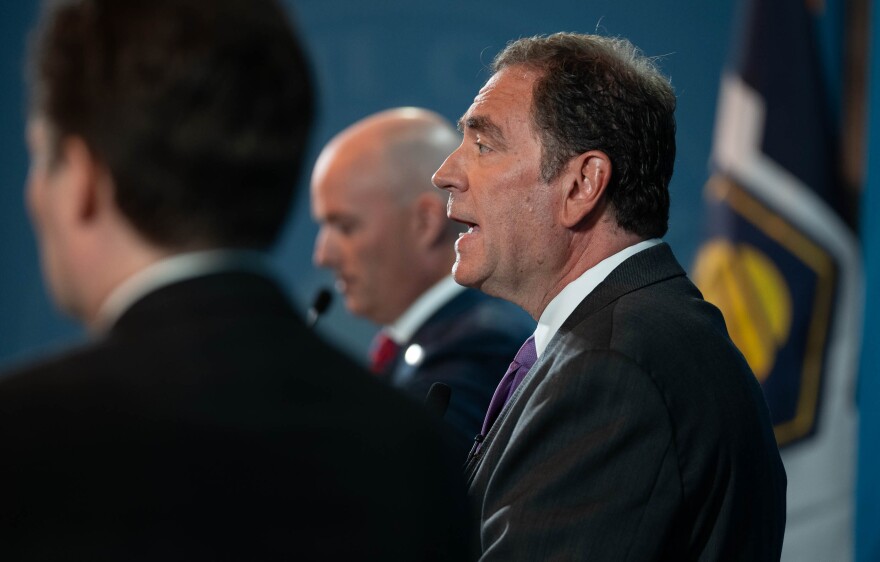A close-up of a man in a suit, standing between two other men in suits.